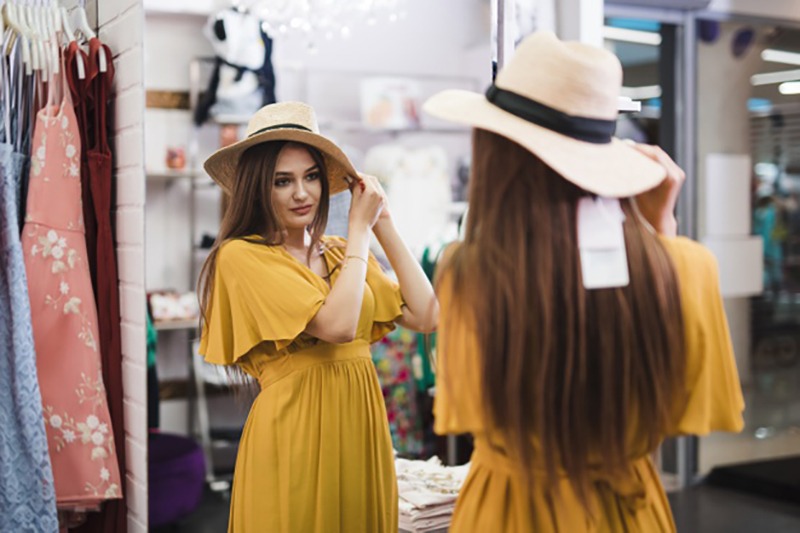Mulher provando um chapéu em frente a um espelho