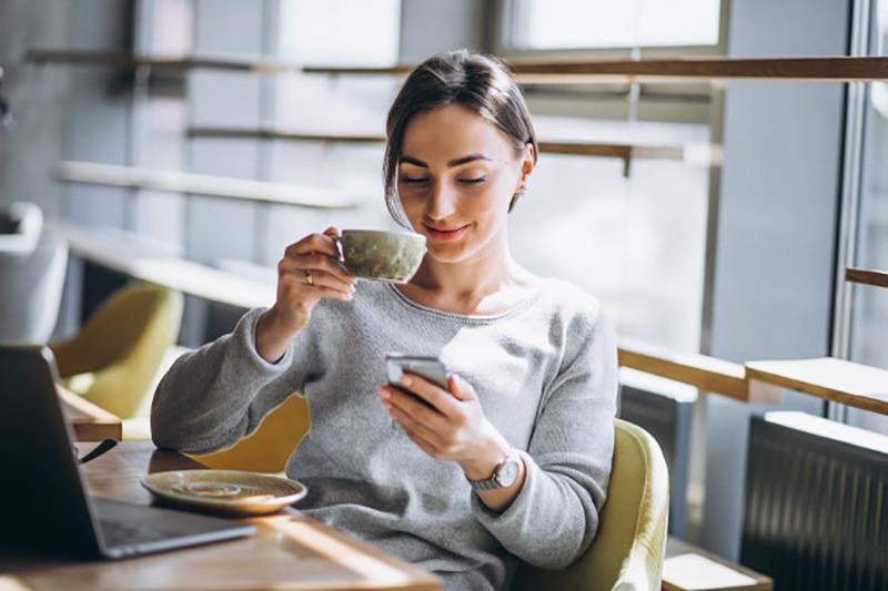 Mulher na jornada do consumidor pelo celular e tomando café