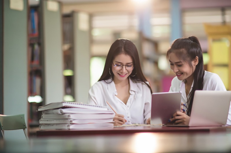 Duas garotas estudando usando livros e plataforma de ensino online